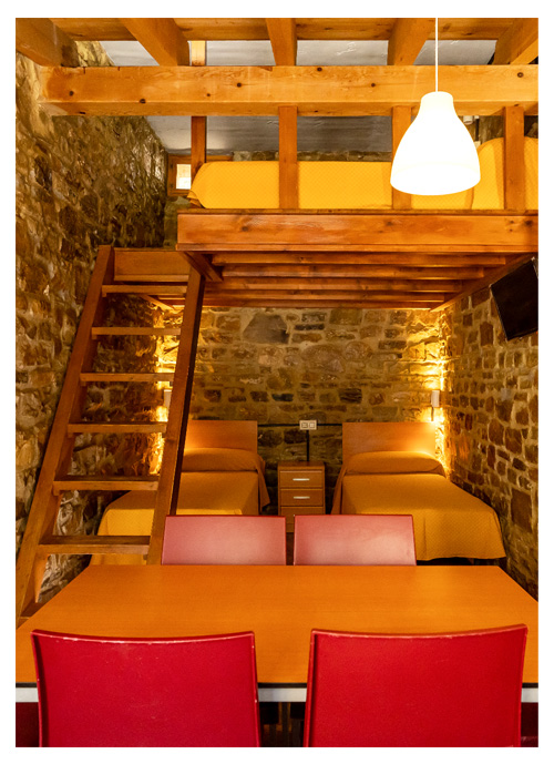 Interior de una de las cabañas de Inturjoven en Cortes de la Frontera, con 4 camas, dos alturas, paredes de piedra, cocina completa, baño y amplia mesa de comedor.