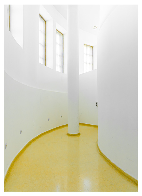 Pasillo blanco y limpio, con suelo amarillo y arquitectura en curva.