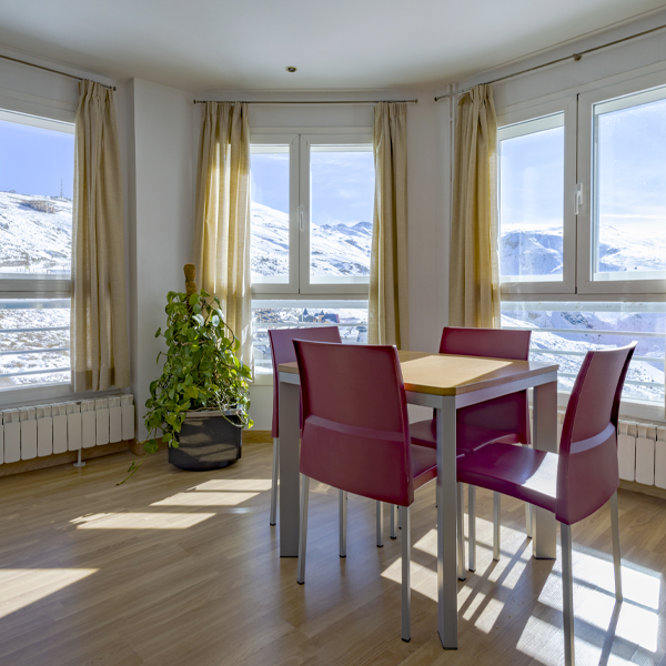 mesa para cuatro en un rincón formado por grandes ventanales con vistas a la sierra.