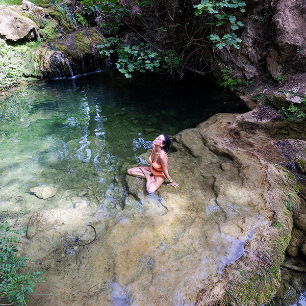 Chica tomando el sol en una roca cerca de un estanque natural